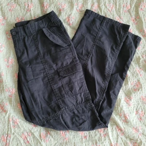 Svarta cargopants med fickor - Säljer ett par svarta cargopants med flera praktiska fickor på sidorna och baktill. Byxorna har normal passform och stängs med knapp och dragkedja. Perfekta för en avslappnad och cool stil.