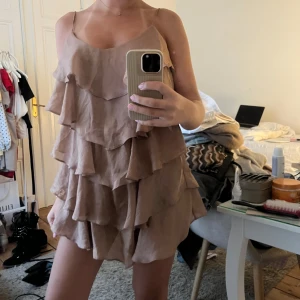 Beige volangklänning med tunna axelband - Säljer en superfin beige klänning med flera lager volanger och tunna axelband. Klänningen har en lös passform och är perfekt för varma dagar. Materialet känns lätt och luftigt.
