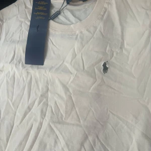 Vit t-shirt från Polo Ralph Lauren - Klassisk vit t-shirt från Polo Ralph Lauren med rund halsringning och broderad logga på bröstet. Enkel och stilren design som passar till det mesta. Mjuk bomullskvalitet för en skön känsla.