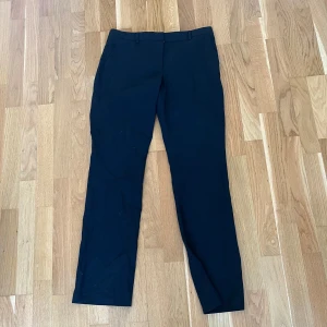 Svarta kostymbyxor med rak passform - Snygga svarta kostymbyxor med klassisk rak passform och diskreta hällor i midjan. Perfekta till en stilren look och passar till många olika outfits. Byxorna har en enkel design utan synliga detaljer framtill.
