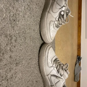Vita Nike Air Force 1 sneakers - Klassiska vita Nike Air Force 1 sneakers med snörning och perforerade detaljer på tån. Skorna har en platt sula och rund tå, samt den ikoniska Nike-loggan på sidan. Perfekta för en stilren och sportig look. Passar till alla kläder! De är lite smutsiga men det går att fixa 