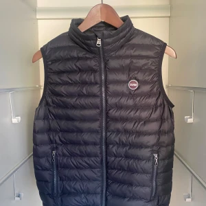 Svart dunväst från Colmar - Säljer en svart dunväst från Colmar med quiltad design och dragkedja framtill. Västen har två fickor med dragkedja och en hög krage. Perfekt för lager-på-lager och stilren look.