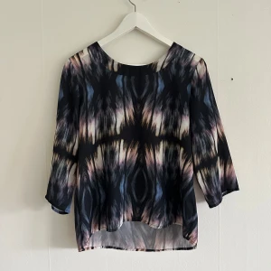 Mönstrad blus med trekvartsärm - Säljer en snygg blus med abstrakt mönster. Blusen har trekvartsärmar och rund halsringning samt dragkedja i ryggen. Perfekt för dig som vill ha något unikt och färgstarkt i garderoben! Utan anmärkningar. 