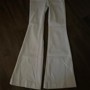 Vita bootcut kostymbyxor - Säljer ett par vita bootcut kostymbyxor med hög midja. Byxorna har en klassisk passform med utsvängda ben och är perfekta för en trendig look. Materialet känns mjukt och bekvämt, och färgen är helt vit. Använda en gång. Innerbenlängd : 75 cm Byxlängd från midjan: 103 cm  Midja: 31 cm 