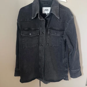 Svart jeans overshirt från Twist & Tango - Säljer en svart overshirt från Twist & Tango i jeansmaterial. Jackan har två stora bröstfickor med lock och knappar, klassisk krage och långa ärmar. Perfekt att slänga över en t-shirt för en cool look. Sparsamt använd vid ett tillfälle . Väldigt fin 