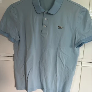 Ljusblå pikétröja från Tiger of Sweden M - Säljer en ljusblå pikétröja från Tiger of Sweden med klassisk krage och knappslå framtill. Tröjan har korta ärmar och en liten broderad tigerlogga på bröstet. Perfekt för en stilren och avslappnad look.