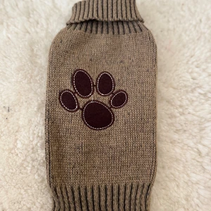 Stickad beige hundtröja med tassmärke - Stickad beige tröja med brunt tassmärke framtill. Perfekt för att hålla värmen under kyliga dagar. Storlek xs
