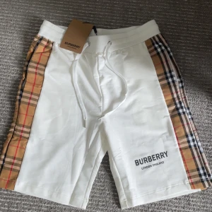 Vita Burberry shorts  - Snygga vita shorts från Burberry med klassiska rutiga paneler längs sidorna och logga framtill. Shortsen har snörning i midjan och är tillverkade i 100% bomull för en mjuk och bekväm känsla. Perfekta för en stilren och trendig look. Köpta i Frankrike, glömde att jag hade de, är nu inte riktigt min stil.