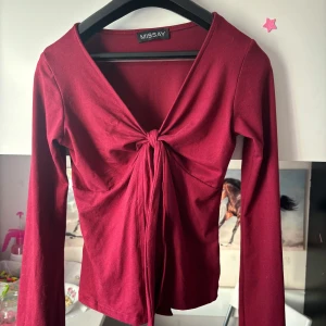 Vinröd långärmad topp med knyt från Missay - Vinröd långärmad topp från Missay med djup v-ringning och knyt framtill. Toppens material är mjukt och stretchigt, perfekt för att skapa en snygg siluett. Enkel men ändå med en fin detalj framtill.