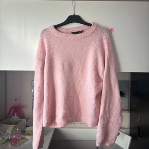 Ljusrosa stickad tröja - Mysig ljusrosa stickad tröja med rund halsringning och långa ärmar. Perfekt för kyligare dagar och enkel att matcha med olika outfits. Tröjan har en avslappnad passform och ribbade muddar vid ärmslut och nederkant.