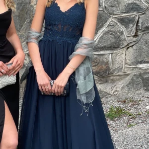 Marinblå långklänning med spets och tyll - Säljer en marinblå långklänning med v-ringad spetsliv och axelbandslös design. Kjolen är i flera lager tyll för en extra elegant look. Perfekt för bal eller fest. Klänningen har öppen rygg och smala axelband.