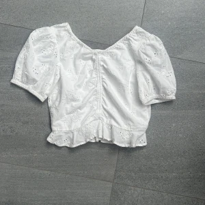 Vit blus från Lindex - Söt vit blus från Lindex med lite blommor och volangkant nertill. Toppen har korta puffärmar och är ganska kort i modellen. Använd en gång!! Skriv vid frågor🩷🩷