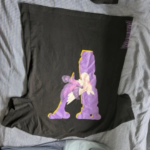 Svart t-shirt från VLONE x Good Intentions - Cool svart t-shirt från VLONE med stort tryck i lila, vitt och gult på både fram- och baksidan. Framsidan har en stor grafisk illustration och baksidan texten 'GOOD INTENTIONS' i fet stil. Perfekt statement-plagg för streetwear. Pris går o diskutera 