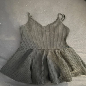 svart ribbad linnetopp - Säljer en svart ribbad linnetopp med smala axelband och v-ringad hals. Toppen har en utsvängd nederdel som ger en söt och avslappnad look. Perfekt att matcha med jeans eller kjol!
