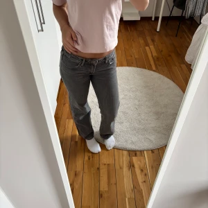 Grå jeansbyxor från Weekday - Säljer ett par grå jeansbyxor från Weekday med låg midja och raka ben. Klassisk femficksmodell med orangea sömmar och knappgylf. Perfekta för en avslappnad stil.