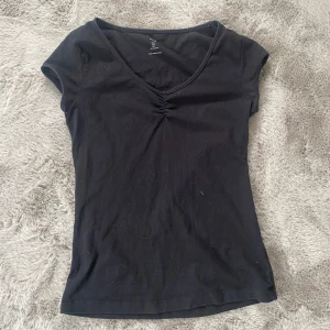 Svart T-shirt  - Säljer en svart T-shirt med liten detalj framtill 