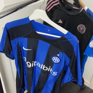 Inter Milan matchtröja - Säljer en blå och svart randig Inter Milan fotbollströja från Nike. Tröjan har korta ärmar och klubbens emblem på bröstet. Perfekt för dig som älskar fotboll och vill visa ditt stöd för laget.