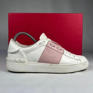 Valentino Open sneakers i vitt och rosa - Säljer ett par snygga Valentino Open sneakers i vitt skinn med en bred rosa skinnpanel över mitten. Skorna har klassisk snörning och rund tå, samt diskreta nitar på hälen. Perfekta för dig som gillar stilrena och exklusiva sneakers.
