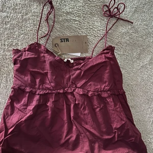 Vinröd topp från Stradivarius - Säljer en vinröd topp i storlek L från Stradivarius med smala knytbara, justerbara axelband. Aldrig använd, prislapp kvar ♥️