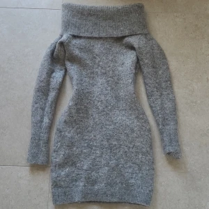 Grå stickad långärmad klänning från H&M - Mysig grå stickad klänning från H&M i mohair- och ullblandning. Klänningen har lång ärm, ribbade muddar och en bred, nedvikt krage som kan användas som offshoulder eller turtleneck. Perfekt för kyliga dagar.