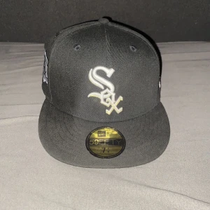 Svart Chicago White Sox keps från New Era - Säljer en svart keps från New Era med Chicago White Sox-logga broderad framtill och ett extra broderat märke på sidan. Klassisk 59FIFTY-modell med platt skärm och strukturerad passform. Perfekt för dig som gillar baseball eller streetwear.