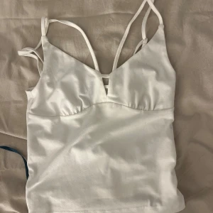 Vit linnetopp med smala axelband - Säljer en stilren vit linnetopp med smala dubbla axelband och v-ringad skärning framtill. Perfekt att matcha med jeans eller kjol för en enkel och fräsch look.
