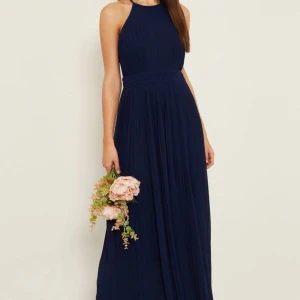 Marinblå långklänning - Marinblå långklänning i halterneck-modell med plisserad kjol och hög halsringning. Klänningen har ärmlös design och markerad midja för en smickrande siluett. Perfekt för bal eller bröllopsgäst/brudtärnor. Jag säljer tre stycken, finns i storlek 10 och 14 (om du tex önskar till fler brudtärnor). Helt oanvända alla tre. Från märket TFNC. 