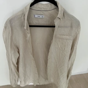 Beige linneskjorta från MNG(mango) - Snygg beige skjorta från mango i 100% linne. Skjortan har klassisk krage, bröstficka och knäppning framtill. 