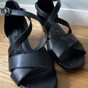 Svarta Klackskor med Spänne - Säljer dessa svarta klackskor som stängs med spänne på sidan. Klacken är 4 cm och de är i väldigt fint skick eftersom att de endast har använts en gång.