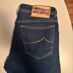 Jacob Cohën blå jeans - Snygga blå jeans från Jacob Cohën med raka ben och klassiska gula sömmar. Jeansen har unika detaljer som broderad text på insidan och patch med motiv bak. Tillverkade i mjukt bomullstyg med knappgylf och logga på myntfickan. Kan gå ner någon hundralapp vid en smidig affär, skambud undanbedes. 