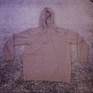 Beige merinoull hoodie  - Beige merinoullshoodie med huva och dragsko. Tröjan har långärmad passform och ribbade muddar vid ärmslut och nederkant. Perfekt för dig som gillar en chill och enkel stil med en touch av klass. Liten defekt som ni ser på slide 2 men syns inte när man har på sig den.