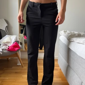 Svarta kostymbyxor med raka ben - Snygga svarta kostymbyxor med klassisk passform och raka ben. Byxorna har hällor för bälte och stängs med dragkedja och knapp. Perfekta till en stilren look och passar till många olika outfits.