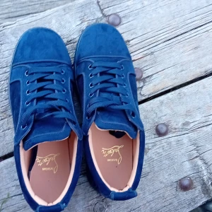 Mörkblå Louboutin - Snygga mörkblå sneakers i mocka från Louboutin. Skorna har klassisk rund tå, snörning och en cool röd sula med logotyp. Insidan är ljusbeige och de har en stilren, enkel design som passar till det mesta.