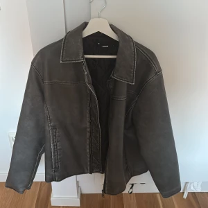 Svart skinnjacka från Bik Bok - Säljer en svart skinnjacka från Bik Bok med klassisk krage och dragkedja framtill. Jackan har raka linjer, två fickor på sidorna och quiltat foder på insidan. Perfekt för dig som vill ha en stilren och edgy look.