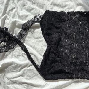 Svart spetsig halterneck tubtopp - Supersnygg svart tubtopp med halterneck och breda spetsband som knyts i nacken. Hela toppen är täckt av mjuk spets med blommigt mönster och har en croppad passform. Perfekt för fest och kanske även halloween som är runt hörnet ❤️🍂🍁