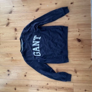 Mörkblå sweatshirt från GANT  - Snygg mörkblå sweatshirt från GANT i klassisk modell med stora vita bokstäver framtill. Tröjan har rund halsringning och långa ärmar, perfekt för en chill och stilren look. Tillverkad i mjuk bomull som känns skön mot huden.