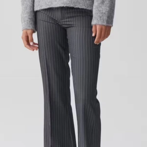 Grå randiga kostymbyxor bootcut - Snygga grå kostymbyxor med smala vita ränder och bootcut-snitt. Byxorna har en klassisk passform med hög midja och raka ben som blir vidare nertill. Perfekta för en stilren look och passar till både stickad tröja och skjorta. Aldrig använda men prislappen kvar!