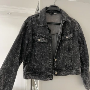 Svart  jeansjacka - Snygg svart jeansjacka med acid wash-effekt och klassisk krage. Jackan har två bröstfickor med knappar, silverfärgade detaljer och raka sömmar. Croppad modell som ger en cool vibe till din outfit. Perfekt för dig som gillar streetstyle.