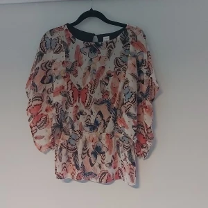 Färgglad blus med fjärilsmönster Lindex - Säljer en luftig blus från Lindex i storlek 146/152. Blusen har ett färgglatt fjärilsmönster i rosa, blått och beige toner, med rund hals och vida ärmar. Perfekt för dig som gillar lekfulla och unika plagg.