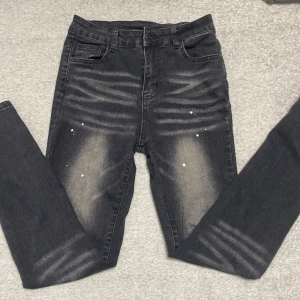 Svarta slim jeans  med slitningar - Snygga svarta skinny jeans med slitna detaljer och ljusa partier framtill. Byxorna har fem fickor, bälteshällor och coola vita färgstänk som ger en trendig look. Perfekta för dig som gillar streetstyle och vill sticka ut lite extra. I storlek 11-12 