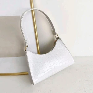 Vit axelväska i croc-mönster - Snygg vit axelväska med croc-mönstrad yta och stilren design. Väskan har en enkel axelrem och stängs med dragkedja. Perfekt för dig som vill ha en clean och trendig look till vardagsoutfiten.