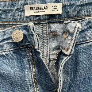 Blåa wide jeans från Pull&Bear - Säljer ett par ljusblå, högmidjade jeans från Pull&Bear i storlek 36. Jeansen har raka, vida ben och klassisk femficksdesign med dragkedja och knapp. Tillverkade i jeansmaterial med snygg tvättad look. Perfekta för en chill och trendig stil.