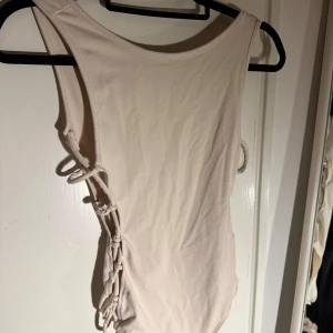 Beige body med snörning från Bik Bok - Supersnygg beige body från Bik Bok i storlek XS. Modellen har cool  snörning längs sidorna som ger en unik look och är tillverkad i mjukt syntetmaterial. 
