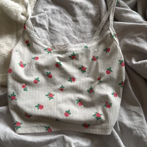 Blommig ribbad linnetopp från SHEIN - Supersöt linnetopp från SHEIN i ljusbeige med små rosa blommor och gröna blad. Toppen har ribbad struktur, smala axelband och spetskant vid halsen för extra gullig vibe. Perfekt för varma dagar och chill outfits.