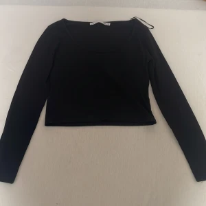 Svart croppad långärmad topp - Svart croppad långärmad topp från 157 med rundad halsringning. Enkel och stilren design som passar perfekt till jeans eller kjol. Mjuk och stretchig känsla, figurnära passform och snyggt kortare längd. Perfekt för dig som gillar minimalistisk stil.