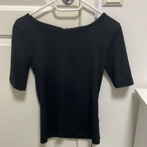 Svart ribbad topp från Gina Tricot - Svart ribbad topp från Gina Tricot i storlek S. Modellen har korta ärmar, rundad hals och en snygg öppen rygg med knytband. Materialet är mjukt och stretchigt, aldrig använnt!