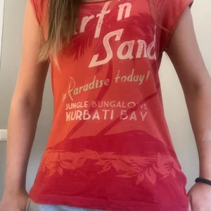 Röd tröja - Snygg röd t-shirt med tryck på framsidan där det står 'Surf n Sand'. ❣️Tyvärr vet jag inte vart tröjan är ifrån, då den legat i garderoben länge😩 Tröjan är i stl M och är då lite loose 😌❣️