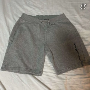 Grå Sail Racing shorts med snörning - Snygga grå shorts från Sail Racing med mjuk känsla och avslappnad passform. De har snörning i midjan, sidofickor och en bakficka. Perfekta för chill dagar eller träning. Diskret logga på benet ger en sportig vibe. 
