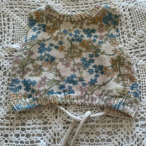 Stickad blommig croppad topp med öppen rygg  - Superfin stickad croptop med blommigt mönster i blått, grönt, rosa och orange på en ljusbeige bas. Toppen är croppad, har öppen rygg och knytdetalj i ryggen. Funkar lika bra på sommaren som vintern! 