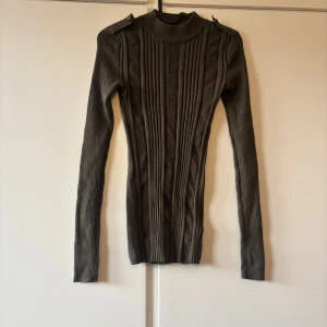 Olivgrön ribbad stickad polotröja XS - Säljer en olivgrön stickad polotröja från Divided by H&M i storlek XS. Tröjan har ribbade detaljer, lång ärm och axelparti med knappar. Snygg och figurnära modell som passar perfekt till höst och vinter.